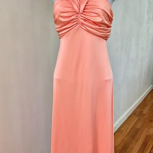 May include: A peach-colored formal gown with a halter neckline and a ruched bodice. The dress is displayed on a white mannequin and has a floor-length skirt. The fabric appears to be a soft, flowing material.