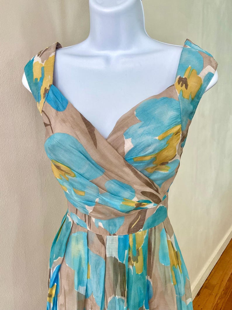 Puede incluir: Vestido sin mangas con estampado floral en tonos azules, amarillos y marrones. El vestido tiene un escote en V y una cintura entallada. La tela parece ligera, adecuada para climas c&aacute;lidos. El vestido mide unos 100 cm de largo.