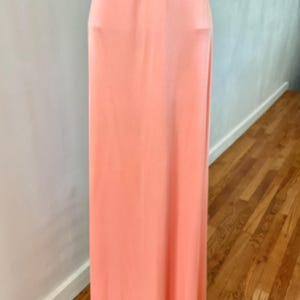 May include: A floor-length, peach-colored dress. The dress has a simple, flowing design with a high waistline. The fabric appears to be a soft, lightweight material. The dress is displayed against a neutral background.