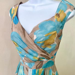 Puede incluir: Vestido sin mangas con escote en V, con un estampado floral en tonos azules, amarillos y marrones. El vestido se exhibe en un maniqu&iacute;, mostrando su dise&ntilde;o. La tela parece ligera, adecuada para climas c&aacute;lidos. Es un vestido de verano.
