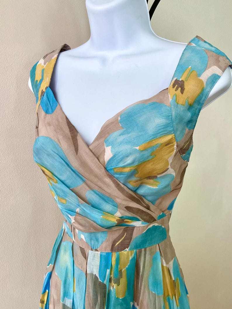 Puede incluir: Vestido sin mangas con escote en V, con un estampado floral en tonos azules, amarillos y marrones. El vestido se exhibe en un maniqu&iacute;, mostrando su dise&ntilde;o. La tela parece ligera, adecuada para climas c&aacute;lidos. Es un vestido de verano.