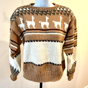 May include: A brown, white, and tan knit sweater with a crew neck. The sweater features a pattern of white llamas, horizontal stripes, and geometric designs. The sleeves and lower hem have a textured knit.
