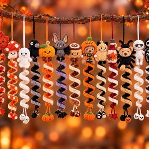 May include: A collection of twelve hanging crochet ornaments featuring Halloween-themed characters including a maple leaf, mushroom, ghost, crow, pumpkin, bat, cinnamon roll, bear in pumpkin suit, cat, potion bottle, spider, mummy, and skeleton.
