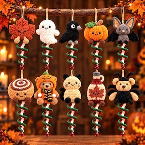 May include: Ten crocheted hanging ornaments featuring autumn and Halloween themes, including a maple leaf, ghost, crow, pumpkin, bat, cinnamon roll, bear in a pumpkin hat, cat, maple syrup bottle, and spider bear, all with spiral tails.