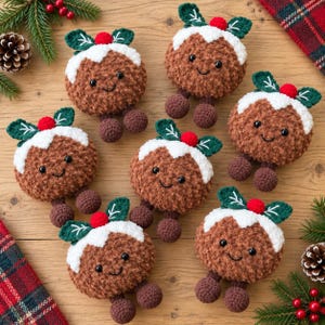 May include: A collection of six brown crocheted Christmas pudding ornaments with white icing tops, green leaves, and small red berries. Each plush figure features black safety eyes and a stitched smile, with two small round feet attached at the base.