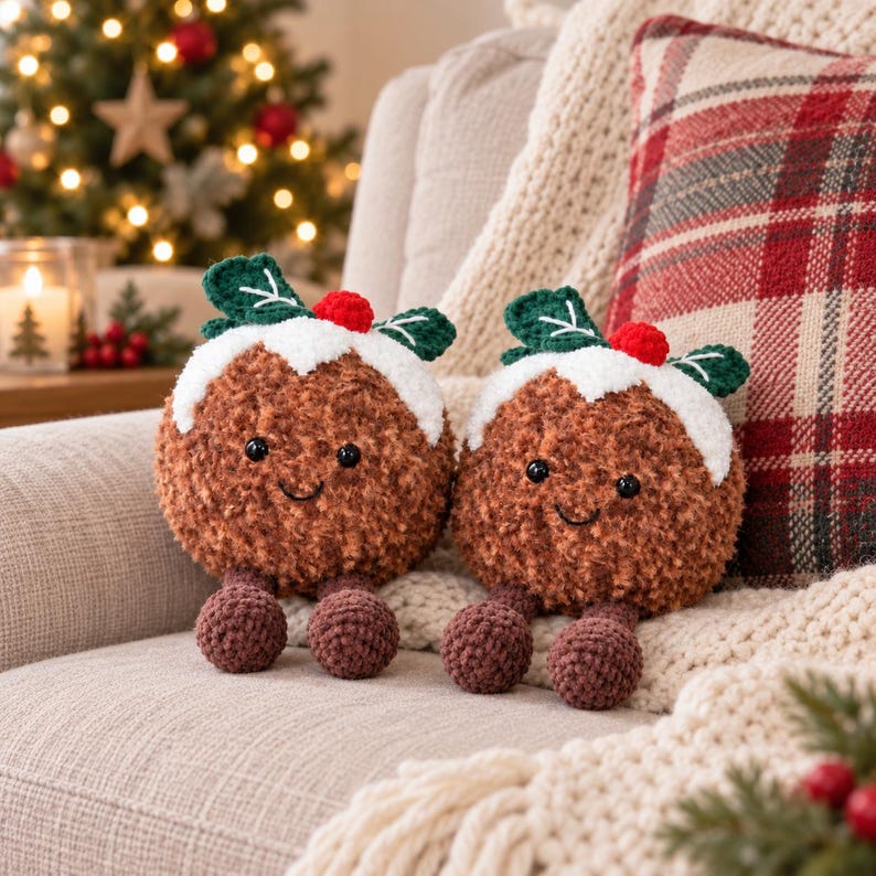 May include: Two round, brown, fuzzy plush toys shaped like Christmas puddings. Each features a white crocheted top, a small red berry, green leaves, black bead eyes, a stitched smile, and two dangling brown crocheted legs with round feet.