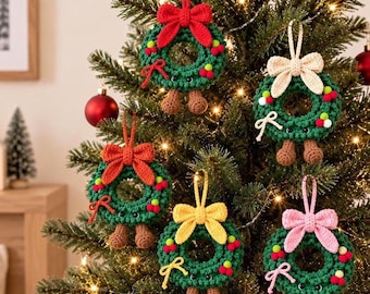 May include: Five crocheted Christmas wreath ornaments hanging on a tree. Each green wreath features a bow, small red and white berries, two brown feet, and a hanging loop. The bows are red, cream, orange, yellow, and pink, with matching small bows.