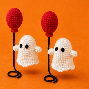May include: Two small, white crocheted ghost figures, each featuring black yarn eyes and outstretched arms. Each ghost is attached to a thin black wire stem that ends in a coiled base, topped with a textured, round, bright red crocheted balloon.