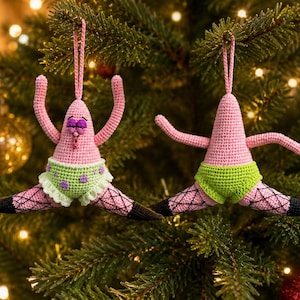 May include: Two crocheted ornaments shaped like a pink starfish character. Each figure wears lime green shorts with purple spots and black fishnet-patterned legs. The figures are posed in a split with arms raised, featuring a hanging loop at the top.