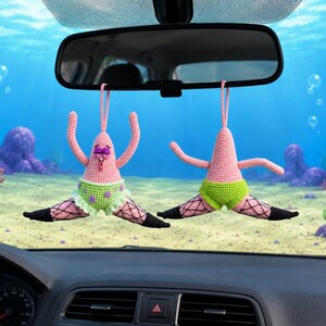 May include: Two crocheted hanging ornaments shaped like a pink starfish character. Each figure wears lime green shorts with purple spots and black fishnet-style leg coverings. The figures are suspended by pink yarn loops from a car rearview mirror.