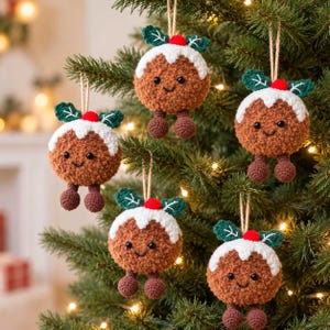 May include: Five round, brown, fuzzy crochet Christmas pudding ornaments hanging from a tree. Each ornament features a white icing top, two green leaves, a small red berry, black bead eyes, a stitched smile, and two dangling brown legs.