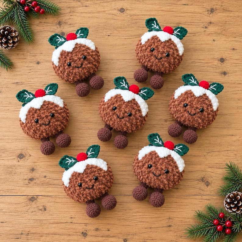May include: Six crocheted Christmas pudding ornaments with brown textured bodies, white icing tops, green leaves, and small red berries. Each pudding features a smiling face with black eyes and two small brown dangling feet.