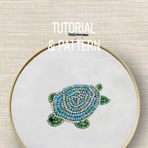 Könnte beinhalten: Ein besticktes Schildkrötenmuster mit blauen, grünen und silbernen Perlen auf weißem Stoff in einem Holzrahmen. Der Text "TUTORIAL & PATTERN" ist oberhalb des Rahmens zu sehen.