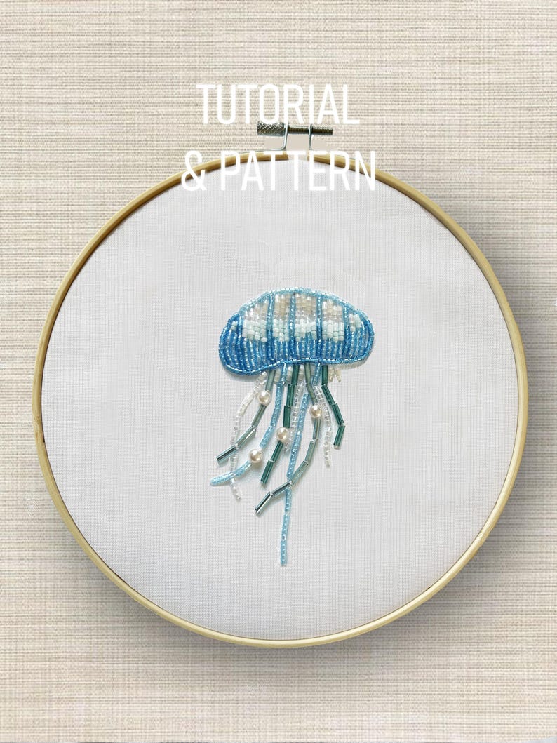 May include: A handmade embroidery hoop featuring a beaded jellyfish design in shades of blue, white, and green. The jellyfish is centered on white fabric, framed by a wooden hoop. Text at the top reads "TUTORIAL & PATTERN".