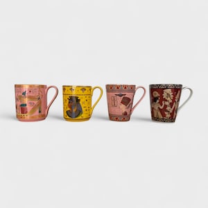May include: Four ceramic mugs with Egyptian designs. The mugs have pink, yellow, and red backgrounds with gold accents and illustrations of pharaohs and hieroglyphs. Each mug has a curved handle.