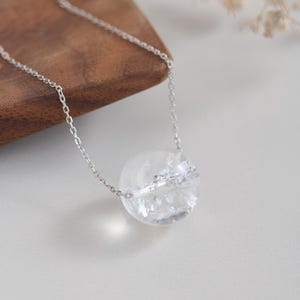 Könnte beinhalten: Eine silberne Kettenkette mit einem Anhänger aus klarem Kristall. Die Kugel hat ein zartes silbernes Design in der Mitte.