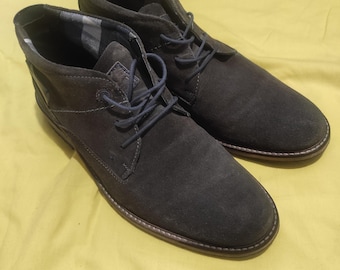 May include: A pair of dark gray suede ankle boots with a lace-up closure. The boots have a brown leather sole and a plaid lining.