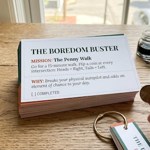 May include: A stack of white and green cards with the text "THE BOREDOM BUSTER" and instructions for a "Penny Walk". A hand holds a coin, with an inkwell and pen nearby. The cards are on a wooden surface.