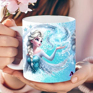 May include: White ceramic mug featuring a vibrant illustration of a character with long, braided white hair, wearing a blue dress, and surrounded by icy blue elements. The mug has a white handle and the letter "A" is visible on the side.