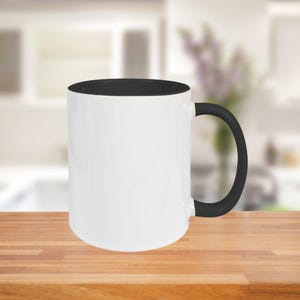 May include: A white ceramic mug with a black interior and handle. The mug is cylindrical and sits on a wooden surface. The background is blurred, suggesting a kitchen setting.
