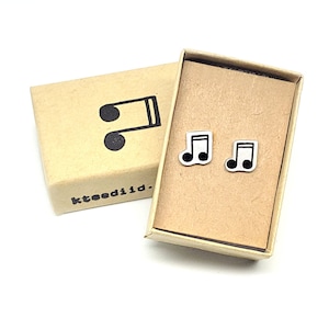 May include: A pair of small, silver musical note earrings in a brown cardboard box. The box has the word "kteeiid." printed on it.