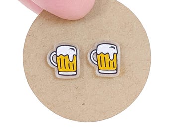 May include: A pair of clear plastic stud earrings with a cartoon image of a beer mug. The mug is yellow with a white foam top and a white outline.