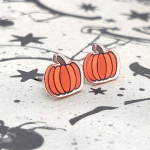 May include: A pair of orange pumpkin stud earrings. The earrings are made of acrylic and have a glossy finish.
