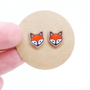 May include: A pair of fox-shaped stud earrings. The earrings are made of clear acrylic with a red and black fox design.