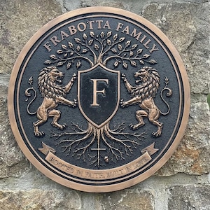 May include: A circular bronze-toned plaque featuring the text FRABOTTA FAMILY at the top and ROOTED IN FAITH, BUILT IN LOVE on a banner at the bottom. The design includes a central shield with the letter F, flanked by two lions and a tree.