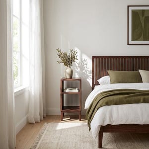 May include: A dark wood bed frame with a slatted headboard, paired with a matching open-shelf nightstand. The bed is dressed in white linens and an olive green throw blanket. A beige vase with green branches sits atop the nightstand.
