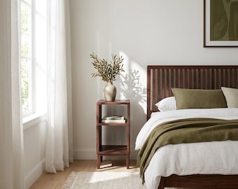 May include: A dark wood bed frame with a slatted headboard, paired with a matching open-shelf nightstand. The bed is dressed in white linens and an olive green throw blanket. A beige vase with green branches sits atop the nightstand.