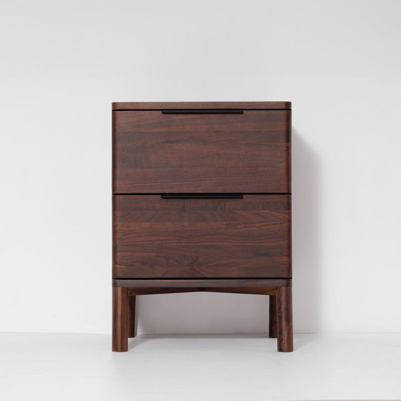 May include: A two-drawer wooden nightstand with a dark brown finish. The nightstand has a rectangular shape with rounded edges and black handles. It stands on four short, sturdy legs.