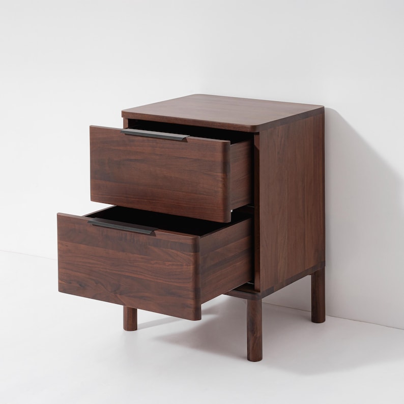 May include: A dark brown wooden nightstand with two drawers, both partially open. The nightstand has a rectangular shape with a flat top and sits on four short legs. The drawer pulls are a dark color, contrasting with the wood grain.