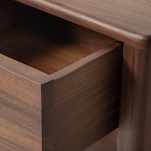 A close-up of the corner of a luxury, heirloom-quality American walnut nightstand with the soft-close drawer open, showcasing meticulous craftsmanship. Rich walnut wood grain and smooth hand-finished surfaces highlight fine detailing and expert joinery, reflecting artisanal craftsmanship in this handcrafted furniture piece. Clean lines and tight-fitting joints emphasize fine workmanship in this compact bedside table.