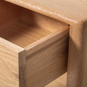 Detailed close-up of a handmade American white oak nightstand, focusing on the open drawer and corner joinery. The small Scandinavian bedside table highlights smooth wood grain, rounded edges, and precise craftsmanship. The natural oak finish and clean lines showcase solid hardwood durability and minimalist handmade wood furniture design, emphasizing modern bedroom storage quality.