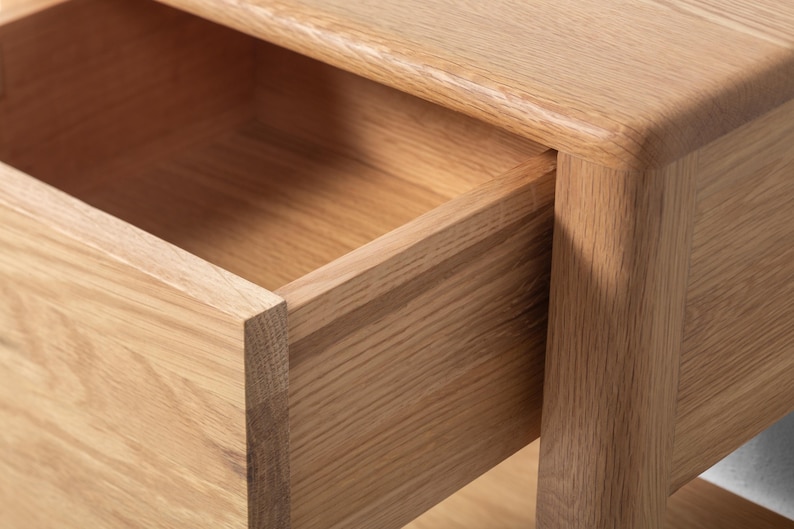 Detailed close-up of a handmade American white oak nightstand, focusing on the open drawer and corner joinery. The small Scandinavian bedside table highlights smooth wood grain, rounded edges, and precise craftsmanship. The natural oak finish and clean lines showcase solid hardwood durability and minimalist handmade wood furniture design, emphasizing modern bedroom storage quality.