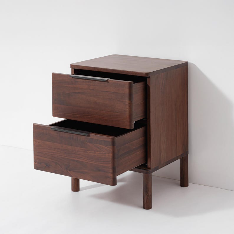 May include: A dark brown wooden nightstand with two drawers, both partially open. The nightstand has a rectangular shape with a flat top and sits on four short legs. The drawer pulls are a dark color, contrasting with the wood grain.