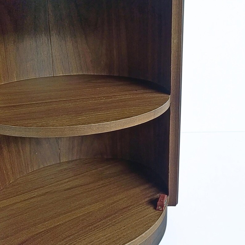 May include: A dark brown, semi-circular wooden shelf unit with two shelves. The shelves are curved and the wood grain is visible. The unit is set against a white background.