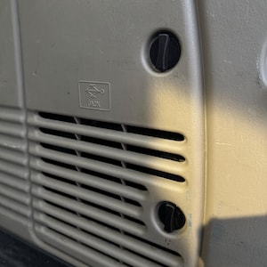 May include: Close-up of a beige car interior panel with a vent and two black knobs. The panel has a small graphic with the word "JACK" printed below it. The panel is made of a textured plastic material.
