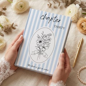 Puede incluir: Un libro de tapa dura con una cubierta a rayas azules claras y blancas. La portada presenta las palabras "chapter THIRTY" en escritura negra, y una ilustración ovalada de flores con el nombre "Alice" en una pancarta. El texto "The best is yet to come" está en la parte inferior.