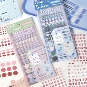 May include: A white ceramic mug with a black handle and the text "But first, coffee" in a handwritten style. The mug is on a white surface. The mug is approximately 4 inches tall.