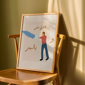 May include: Framed art print featuring a stylized illustration of a person pouring blue liquid from a container. The artwork includes Arabic text in brown and gold tones, set against a beige background. The frame is made of light-colored wood.