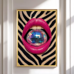 May include: A framed wall art print featuring a pair of vibrant hot pink lips slightly parted to hold a reflective, multi-colored disco ball. The background consists of a black and beige zebra stripe pattern, all enclosed in a thin gold frame.