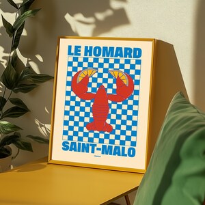 Peut inclure: Une affiche encadrée avec une illustration de homard rouge et des tranches de citron, sur un fond à carreaux bleu et blanc. Le texte "LE HOMARD SAINT-MALO" est affiché en bleu. L'affiche est dans un cadre doré.
