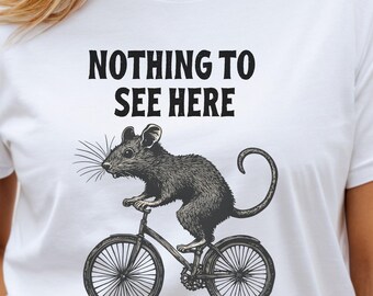 May include: White t-shirt with a black and white illustration of a rat riding a bicycle. The text "Nothing to see here" is printed on the shirt.