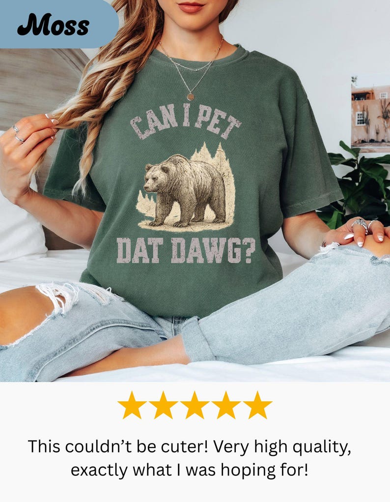 May include: Moss green t-shirt with the phrase "CAN I PET DAT DAWG?" and a graphic of a bear. The shirt is a relaxed fit and has a vintage style. The text and bear graphic are in a distressed style.
