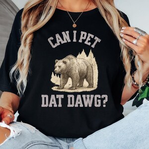 May include: Black t-shirt with the text "CAN I PET DAT DAWG?" above and below a graphic of a bear walking in front of a mountain silhouette. The shirt is a solid black color.