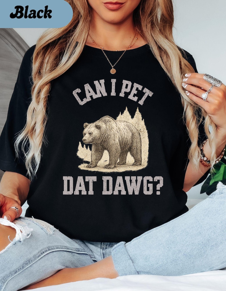 May include: Black t-shirt with the text "CAN I PET DAT DAWG?" above and below a graphic of a bear walking in front of a mountain silhouette. The shirt is a solid black color.