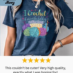 May include: Heather navy t-shirt with the text "I Crochet favorite hobby collecting YARN" and colorful yarn balls. The shirt features a crew neck and short sleeves. The design includes a crochet hook and the word "YARN".