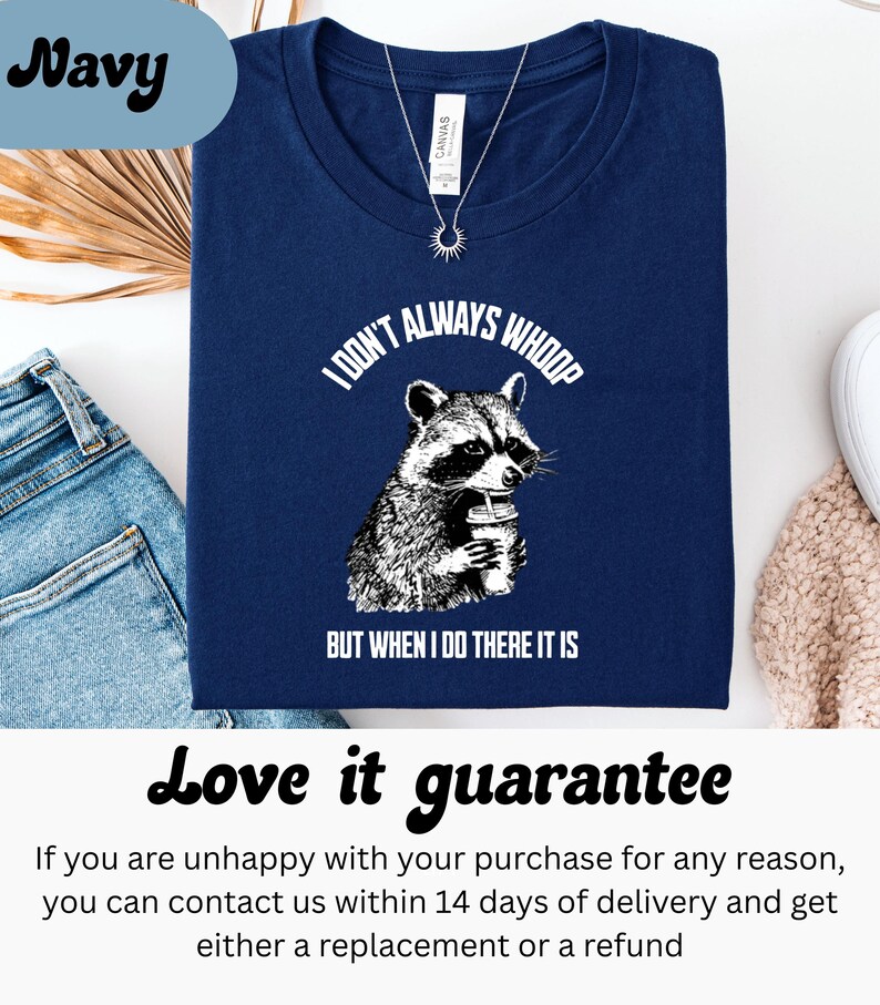 May include: Navy blue t-shirt with a graphic of a raccoon holding a cup, and the text "I DON'T ALWAYS WHOOP BUT WHEN I DO THERE IT IS". The shirt is next to a pair of blue jeans.